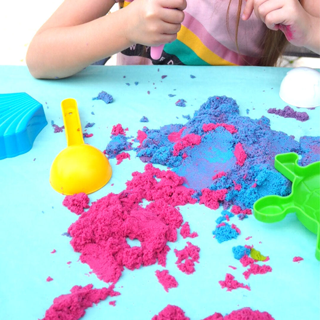 Kinderhanden spelen met roze en blauw kinetisch zand en een geel schepje.