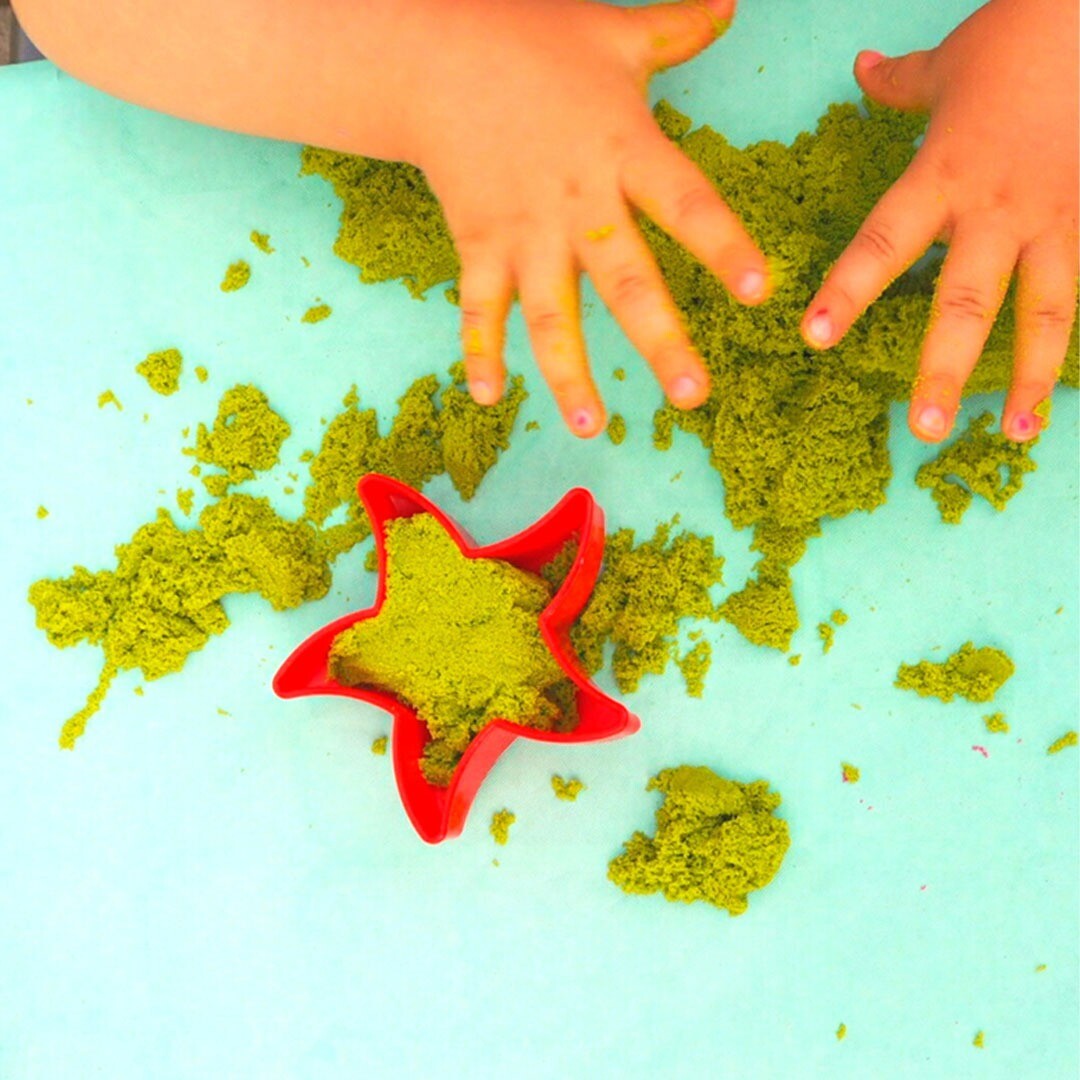 Kinderhanden spelen met groen kinetisch zand, met een rode stervormige uitsteker gevuld met zand.