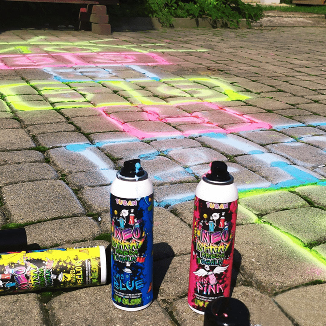 Drie Tuban Neo krijtspray spuitbussen in blauw, roze en geel naast een kleurrijke hinkelbaan.