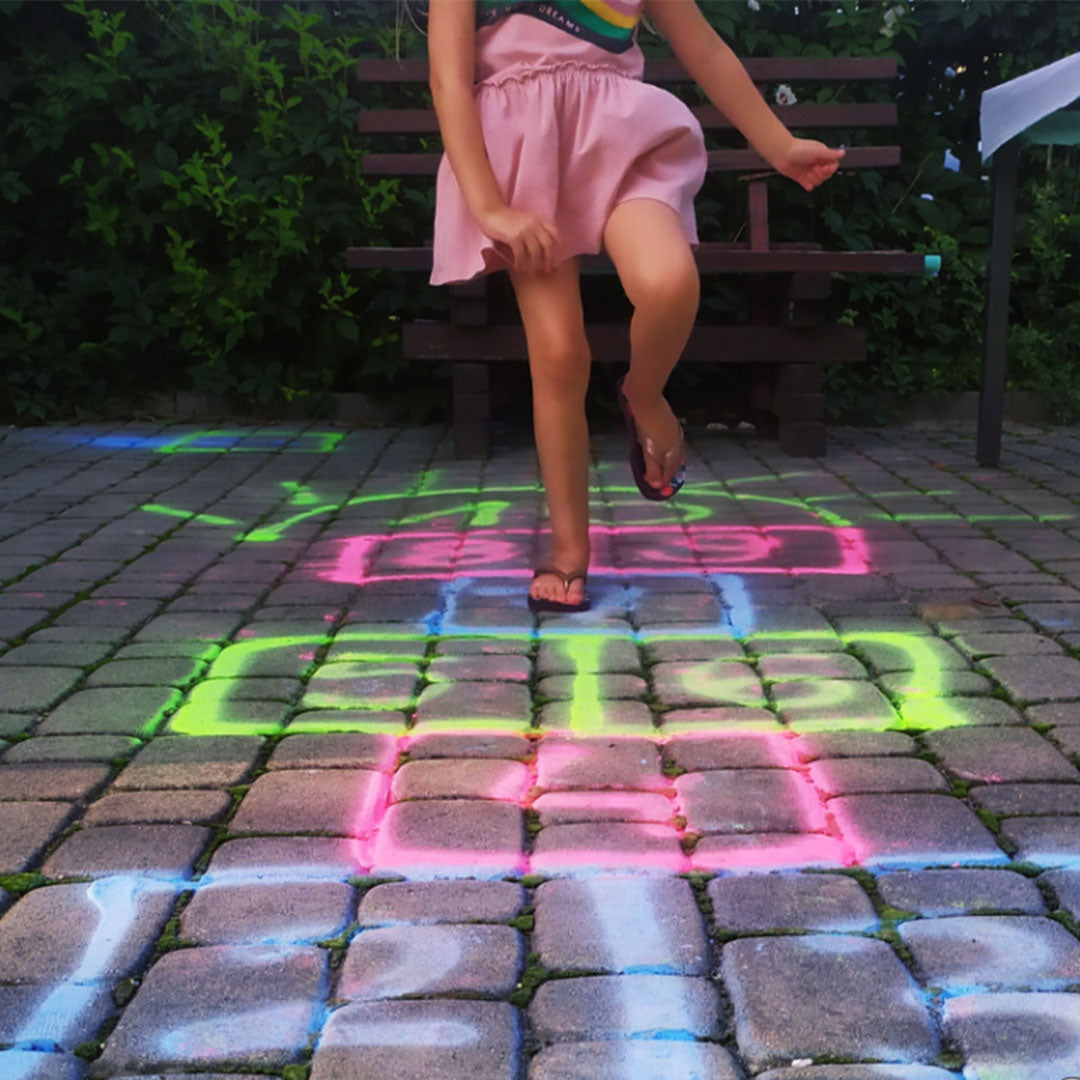 Een kind speelt hinkelspel op een terras met een kleurrijk krijtpatroon gespoten met krijtspray.