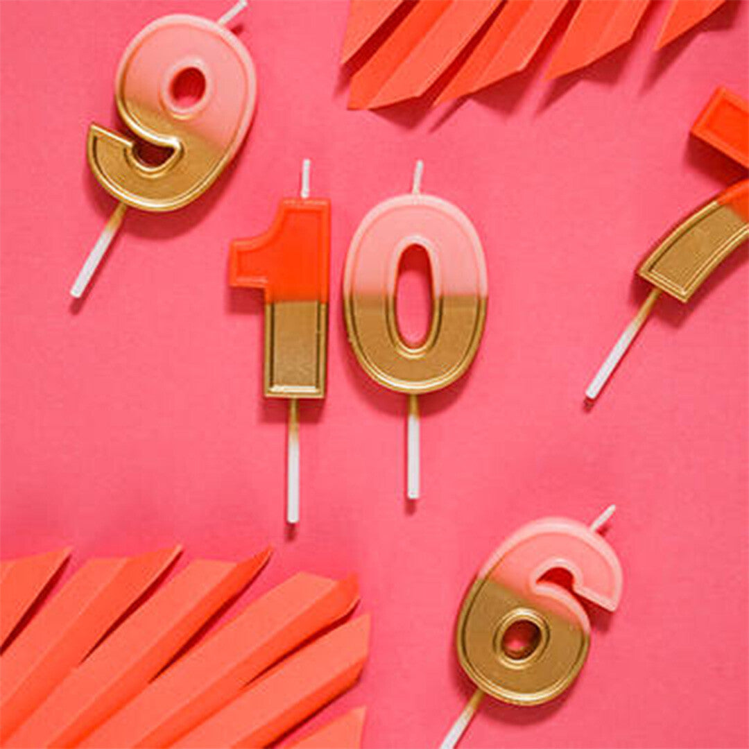 Collectie roze gouden verjaardagskaarsen in de vorm van de cijfers 9, 10 en 6 op een roze achtergrond.