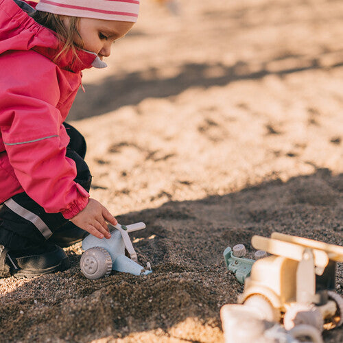 Een kind speelt met een Viking Toys lichtblauwe plastic speelgoedhelikopter in het zand.
