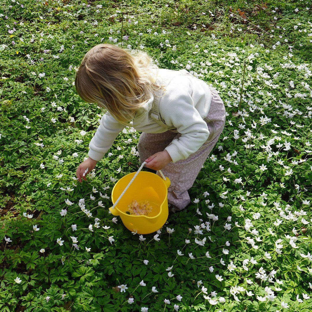 Kind plukt bloemen in een veld met de gele Viking Toys emmer.