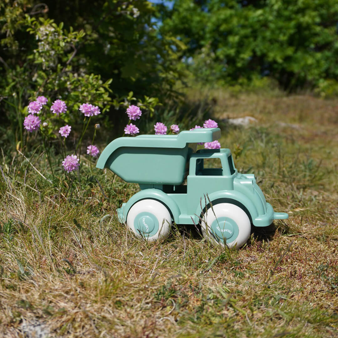 Viking Toys groene plastic speelgoed kiepwagen in het gras met roze bloemen op de achtergrond.