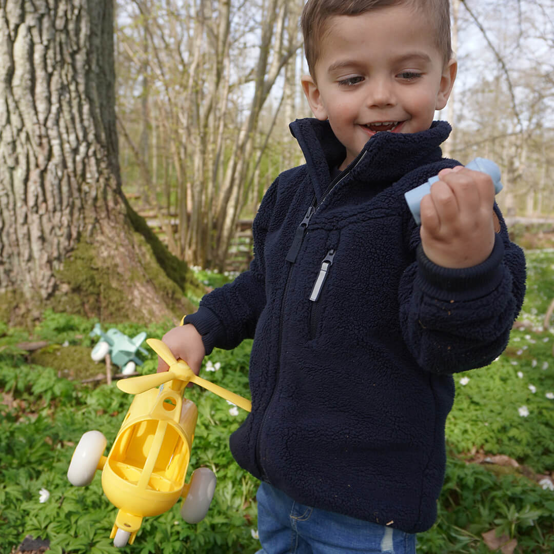 Een lachende jongen speelt met de gele speelgoedhelikopter in een bos.