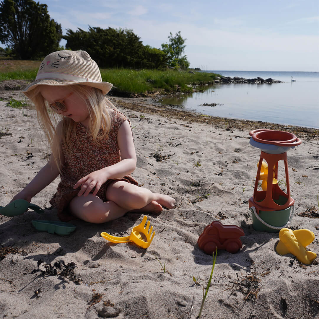 Een kind speelt met de Viking Toys re:line zand- en watermolen en ander strandspeelgoed op een zandstrand.