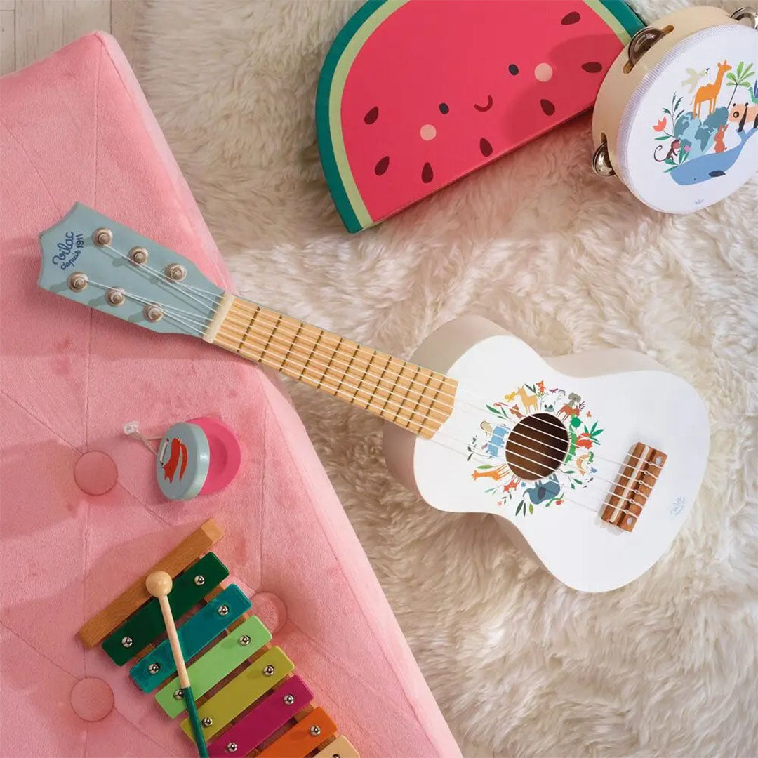 Vilac speelgoedgitaar met dierenillustraties, samen met andere muziekinstrumenten op een roze stoel en wit kleed.