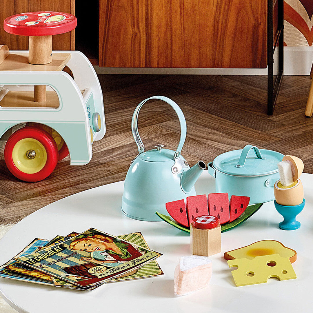 Een deel van de Vilac houten ontbijtset op een witte tafel, met een watermeloen, ei in eierdop, toast en kaas.
