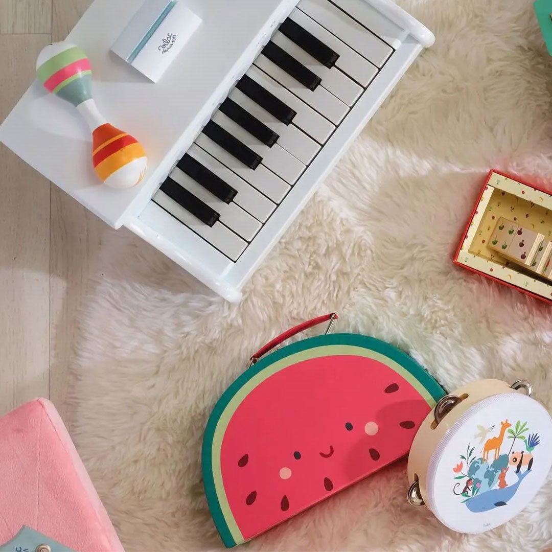 Bovenaanzicht van de Vilac houten speelgoedpiano met andere muziekinstrumenten op een witte vloerbedekking.
