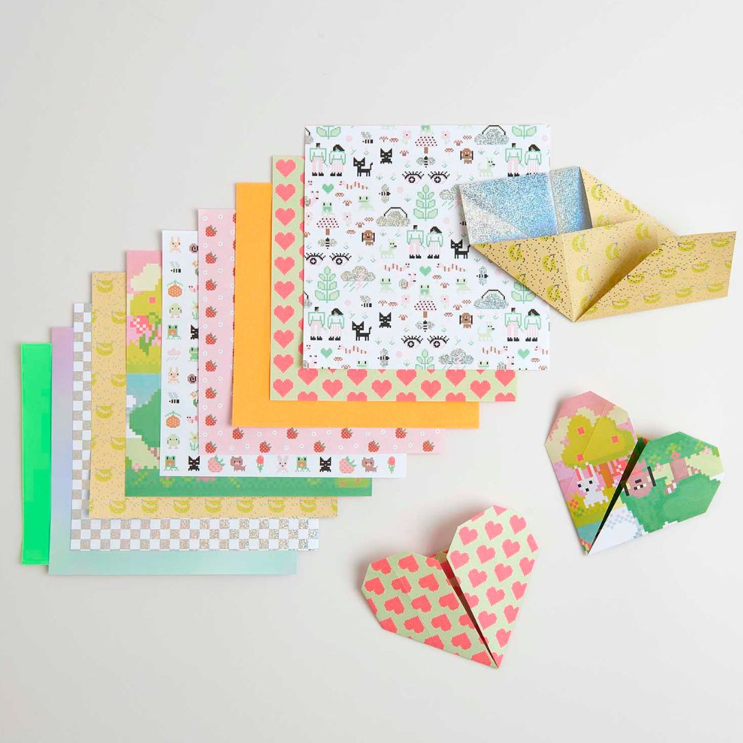 Een stapel Rico Design origami papier met diverse patronen, deels gevouwen tot twee harten en een boot.