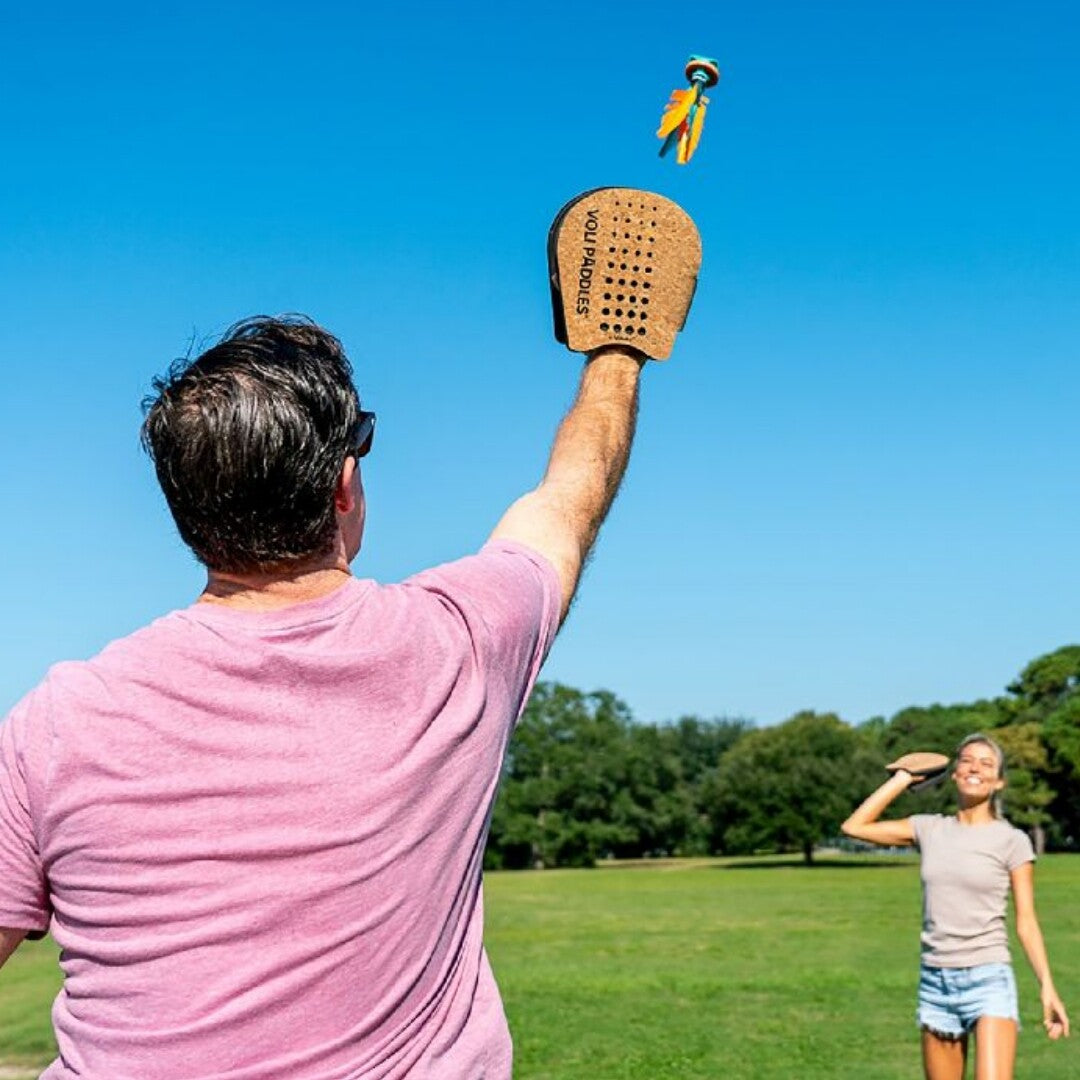 Een persoon speelt buiten met een Waboba Voli Paddle en een shuttlecock in een park.