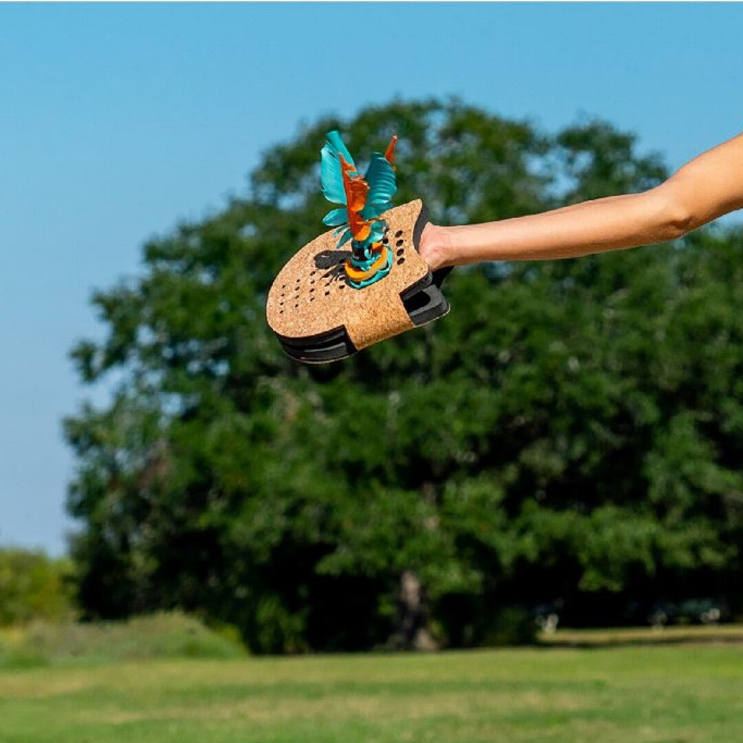 Een hand houdt een Waboba Voli Paddle vast met een shuttlecock erop, buiten in de natuur.