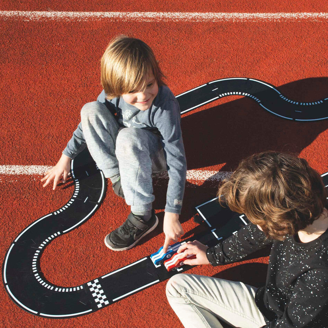 Twee kinderen spelen met de waytoplay rubberen racebaan en speelgoedauto's op een rode ondergrond.