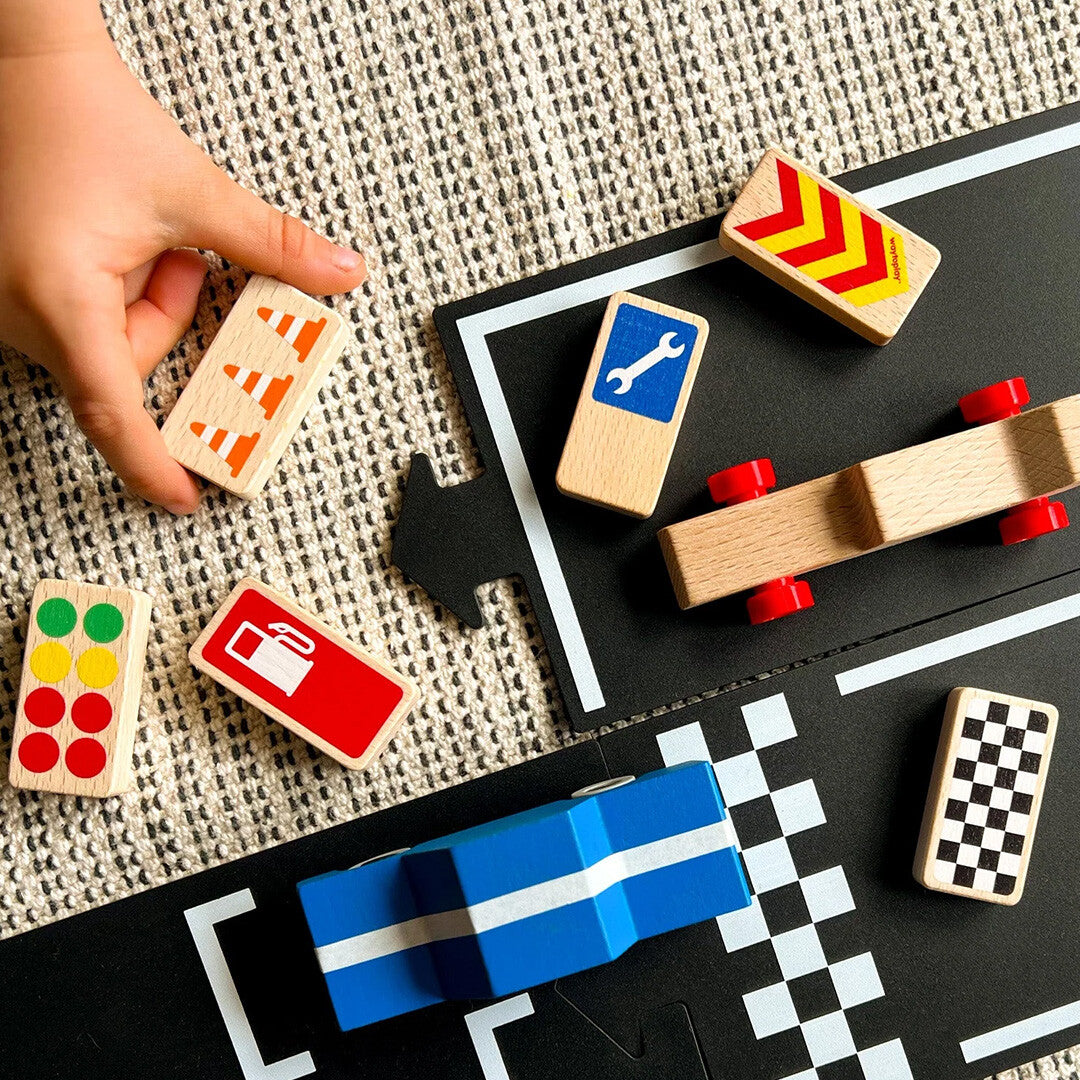 Een kinderhand speelt met waytoplay houten raceborden en een blauwe speelgoedauto op een zwarte racebaan.