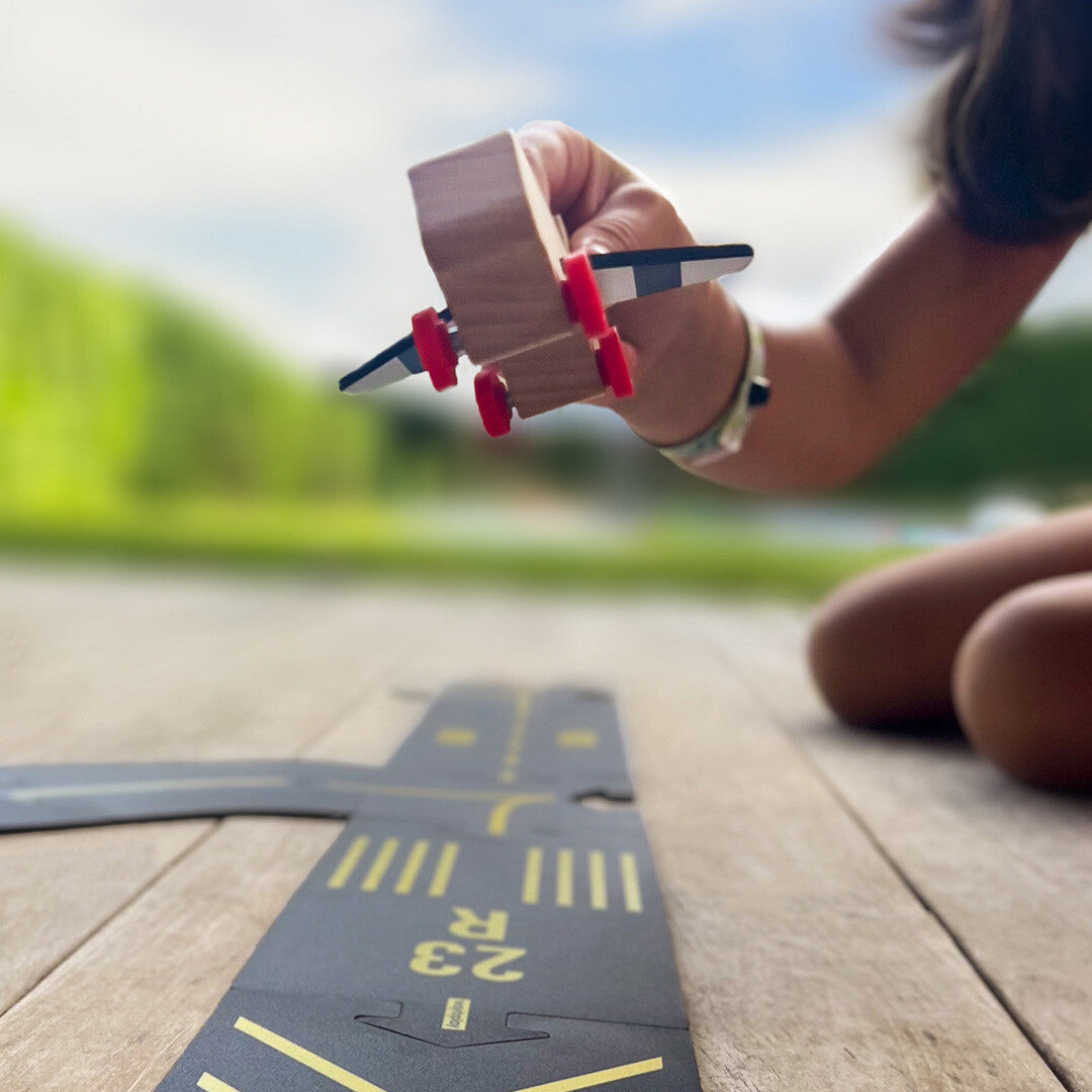 Een kind houdt een houten vliegtuigje in de lucht boven een waytoplay runway speelbaan.