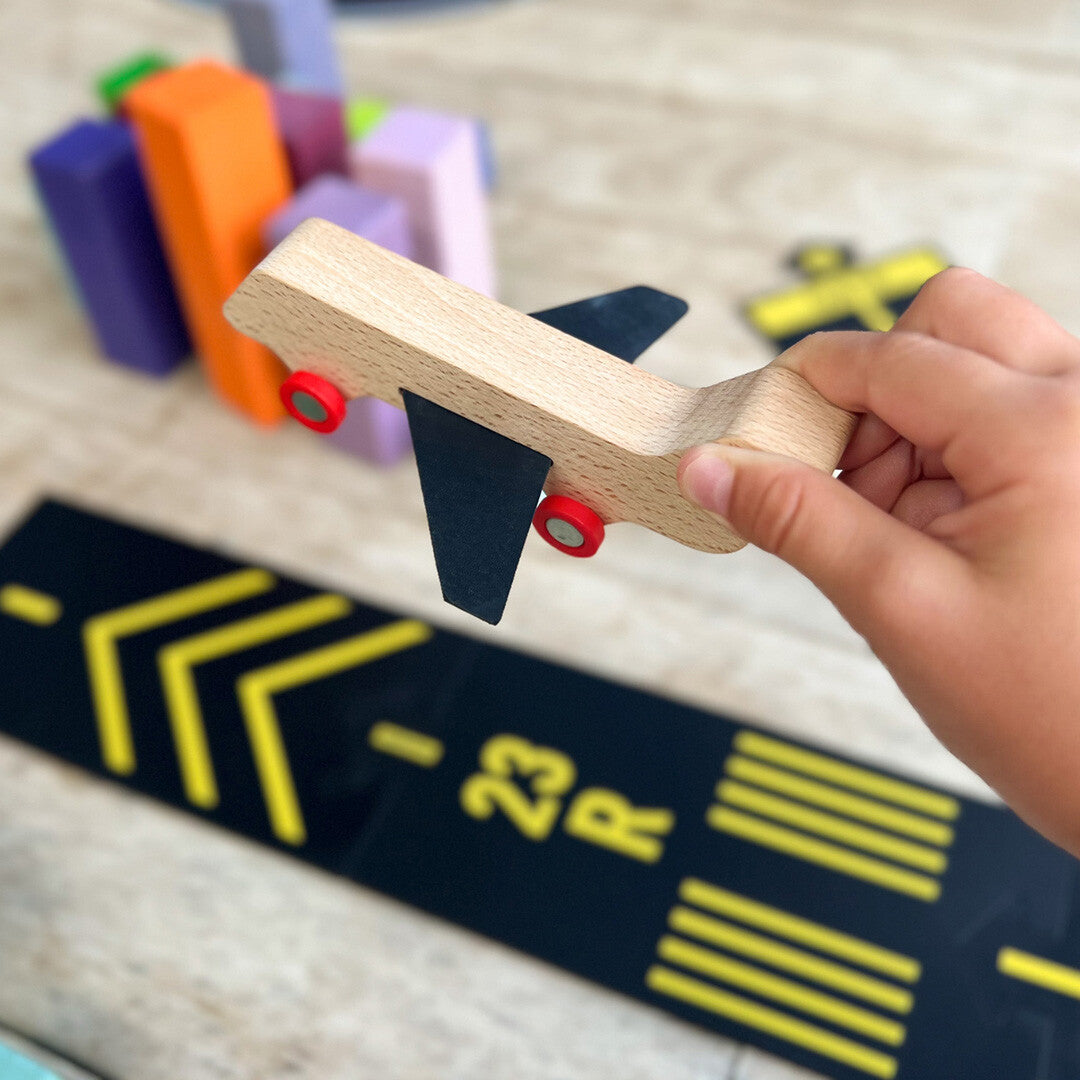 Een hand houdt een houten vliegtuigje vast boven een waytoplay runway speelbaan.