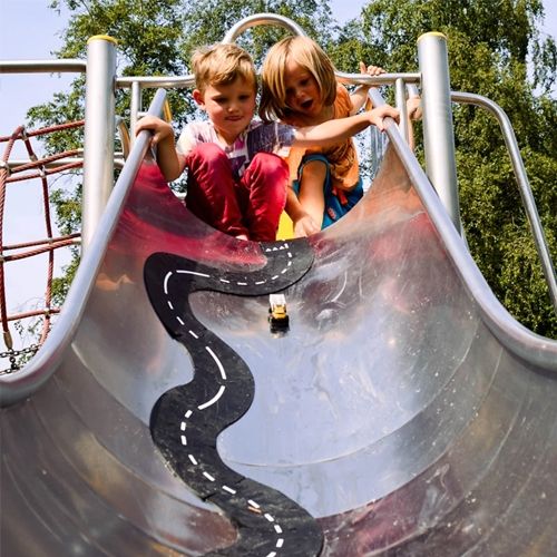 Twee kinderen spelen met een waytoplay rubberen wegdeel en een speelgoedauto op een glijbaan.