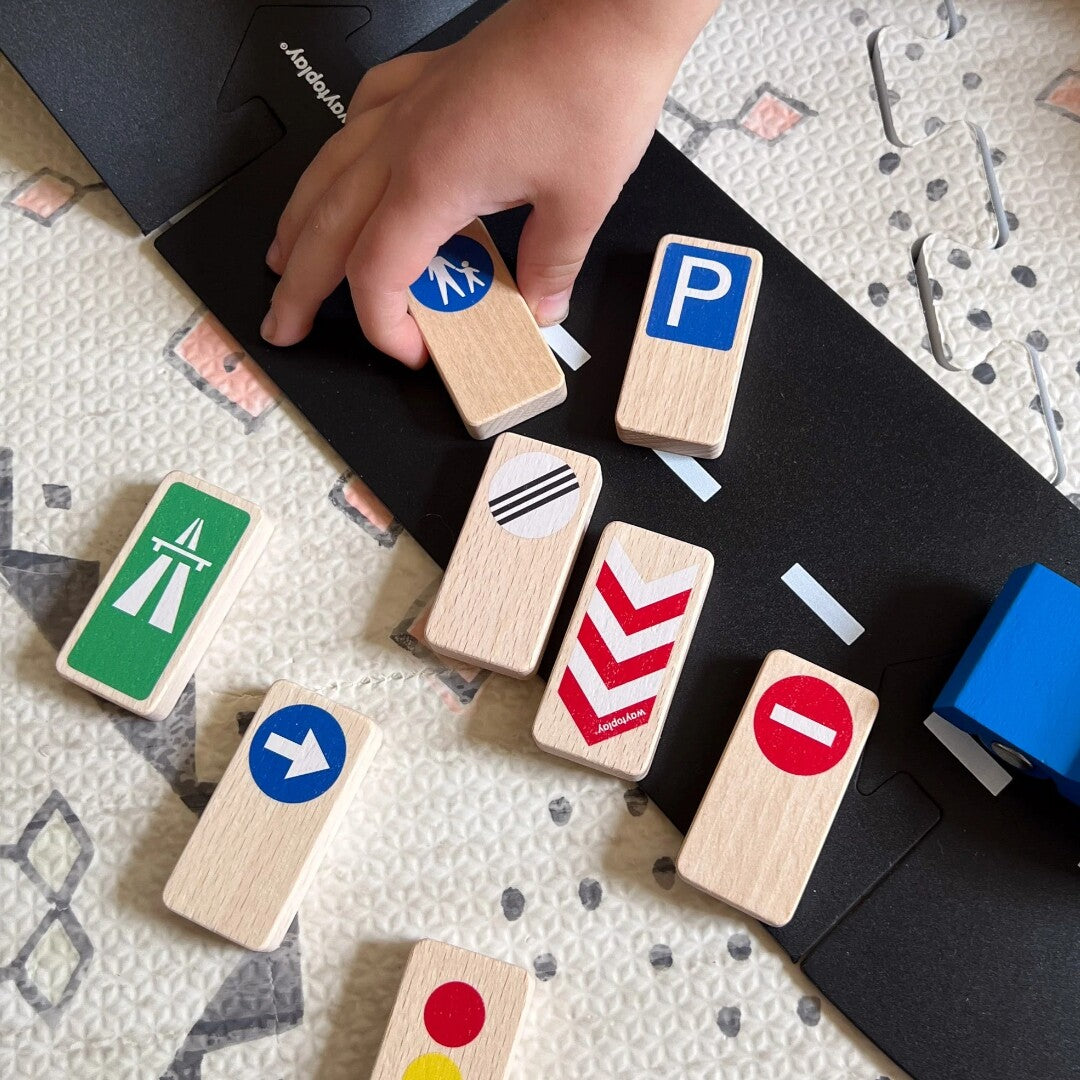 Een kinderhand pakt waytoplay houten verkeersborden speelgoed van een speelmat met een weg.