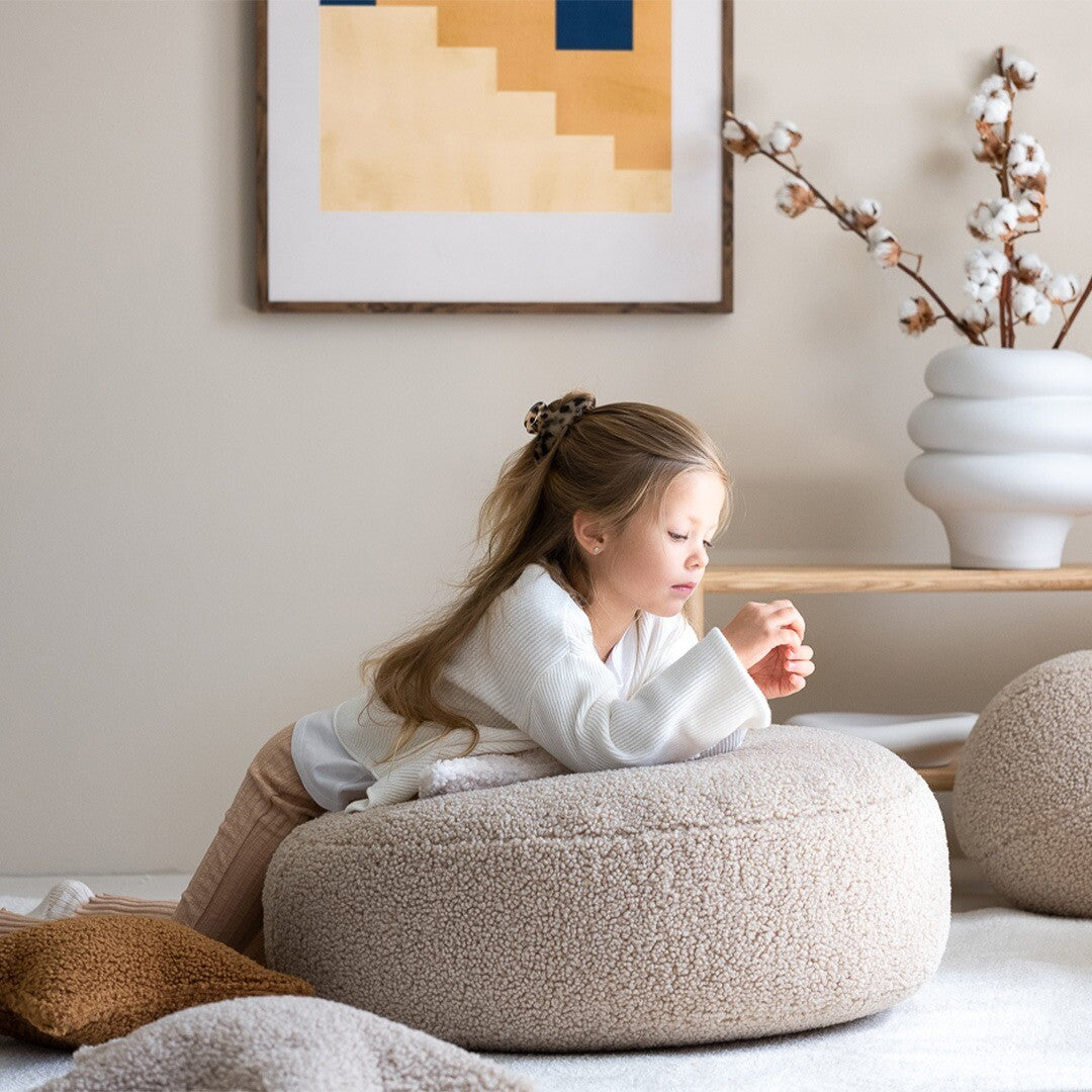 Een meisje leunt op de wigiwama beige poef in een kinderkamer.