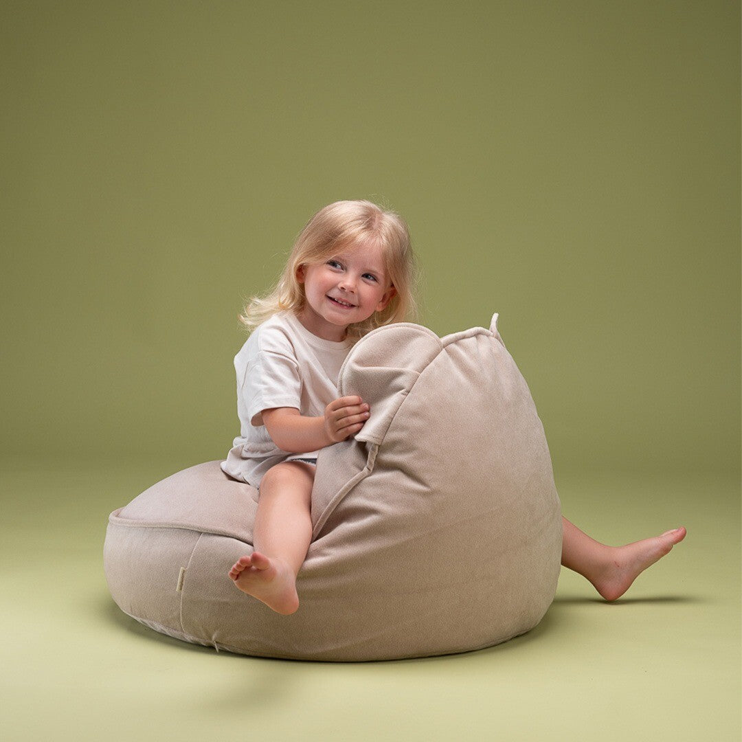 Een blond meisje zit lachend schuin in de wigiwama beige fluwelen zitzak met berenoren.