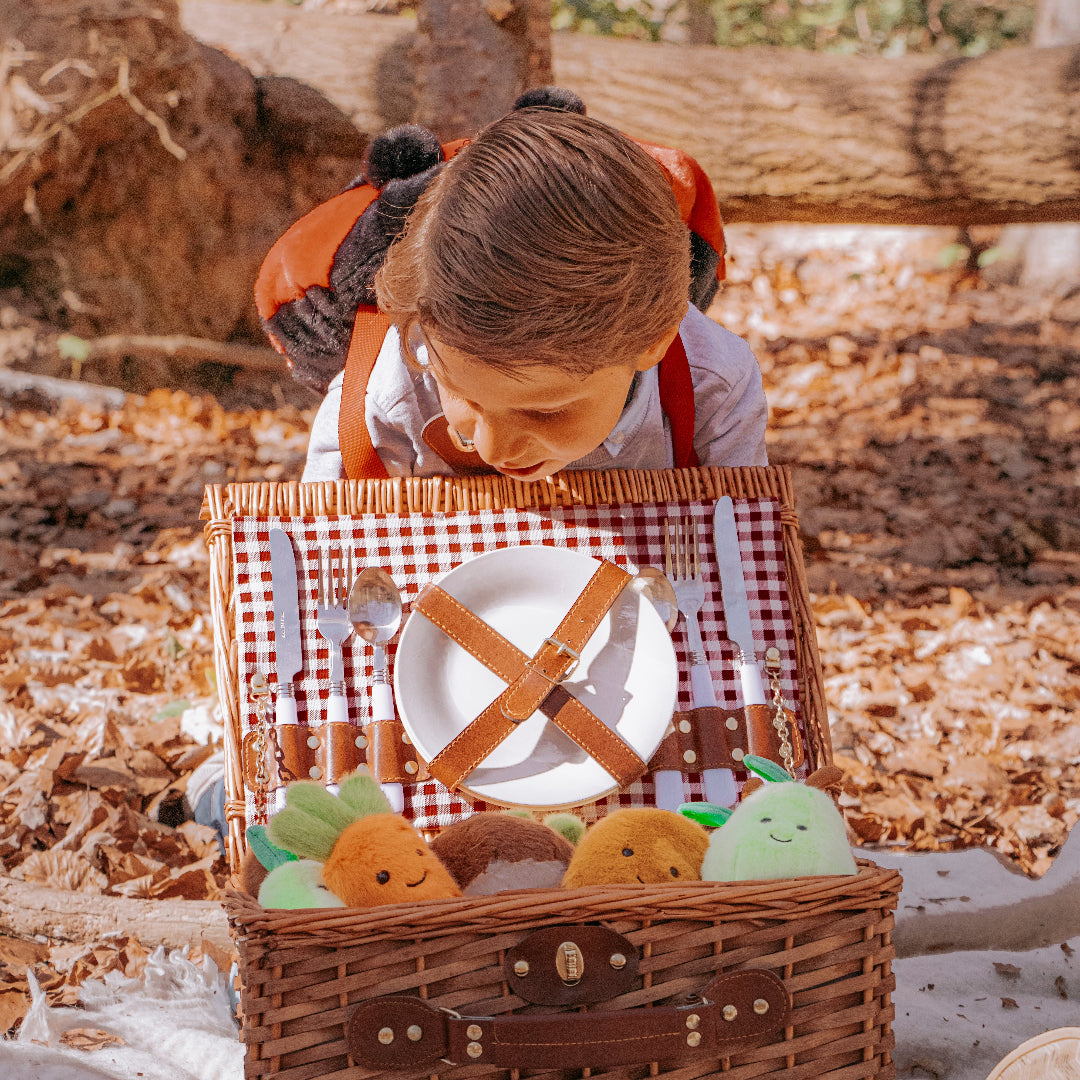 Een kind met een lieveheersbeestje rugzak kijkt in een picknickmand met pluchen groente- en fruitknuffels.
