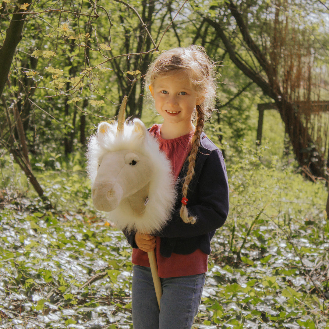 Een lachend meisje houdt de Wild & Soft stokdier eenhoorn vast in een bos.