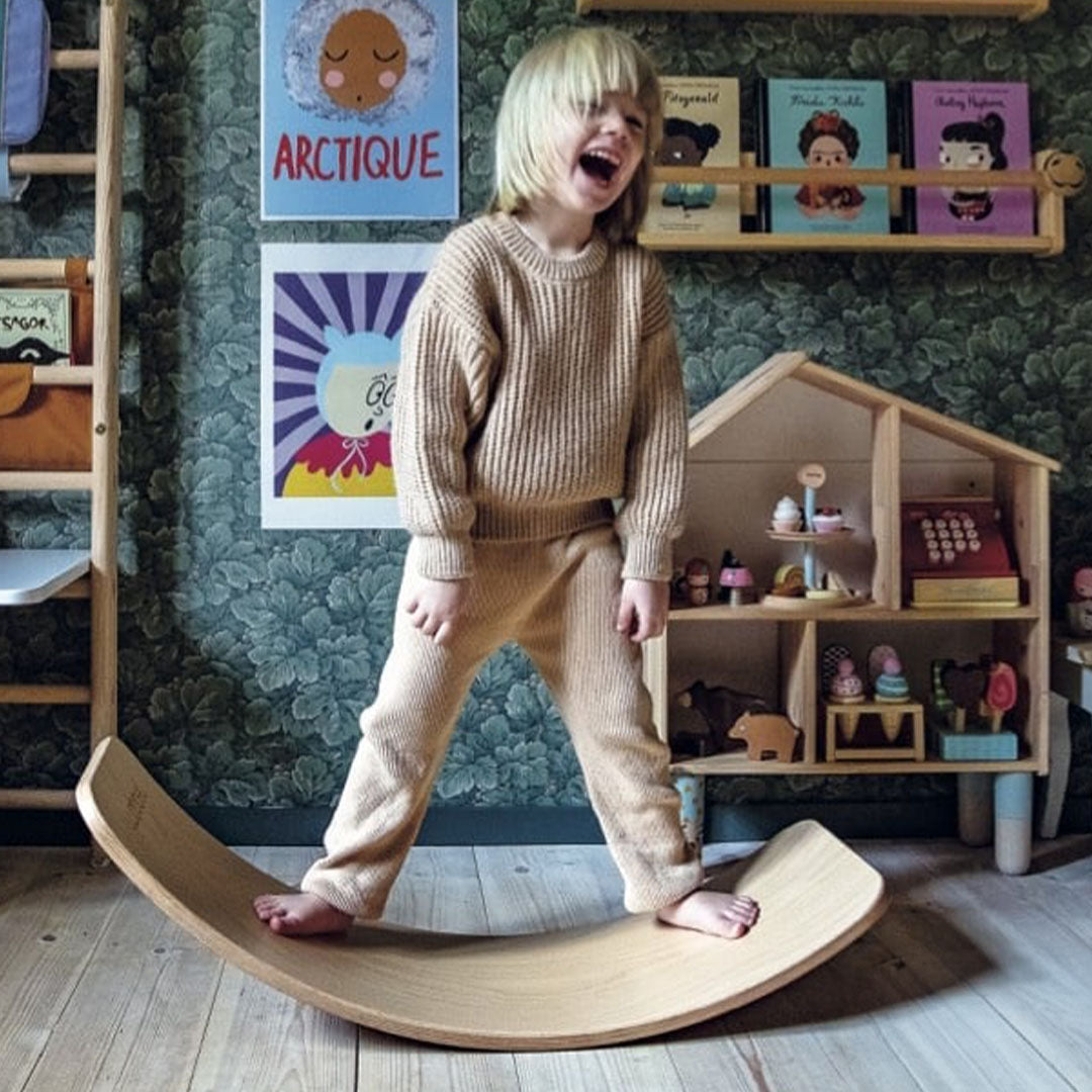 Een lachend kind balanceert op een Wobbel balansbord van hout.