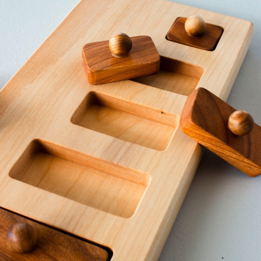 Close-up van de Wooden Story houten knoppuzzel, met lege sleuven en enkele bruine houten blokjes met knop.