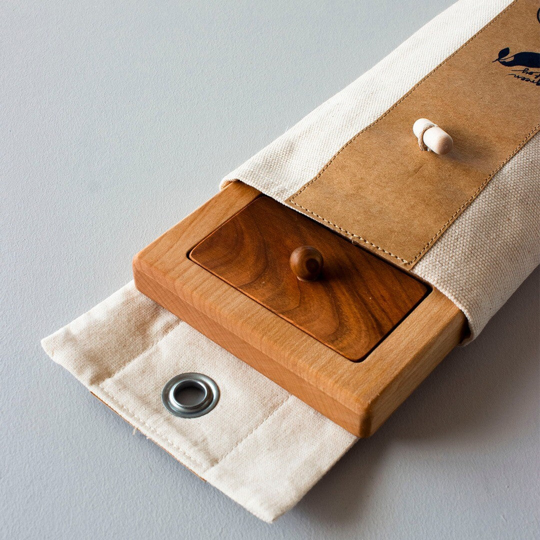 De Wooden Story houten knoppuzzel deels in een linnen opbergzak met een bruine flap.