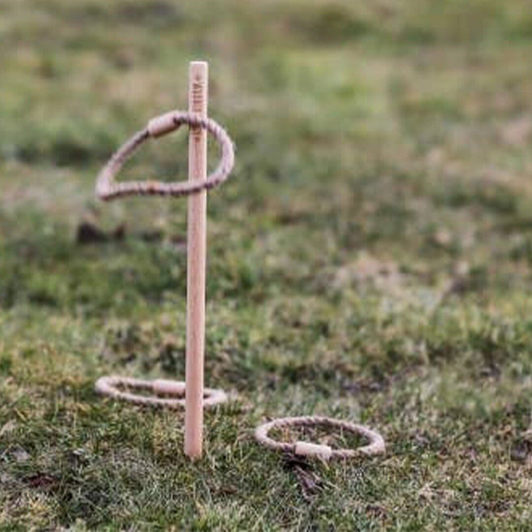 Een houten pin van het luswerpen behendigheidsspel staat in het gras met een touwring eromheen en een ring ernaast.