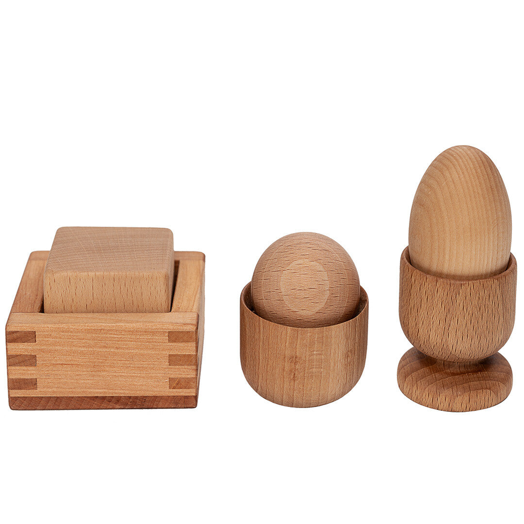 Drie houten Montessori sorteervormen, waaronder een blok, een bol en een ei, op een witte achtergrond.