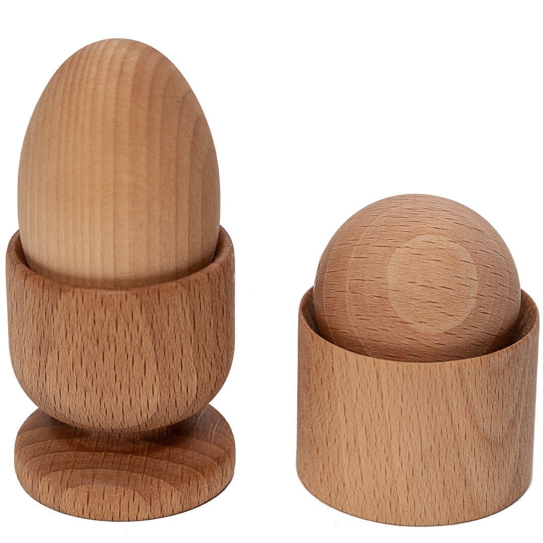 Twee houten Montessori sorteervormen, een ei in een eierdop en een bol in een cilinder, op een witte achtergrond.