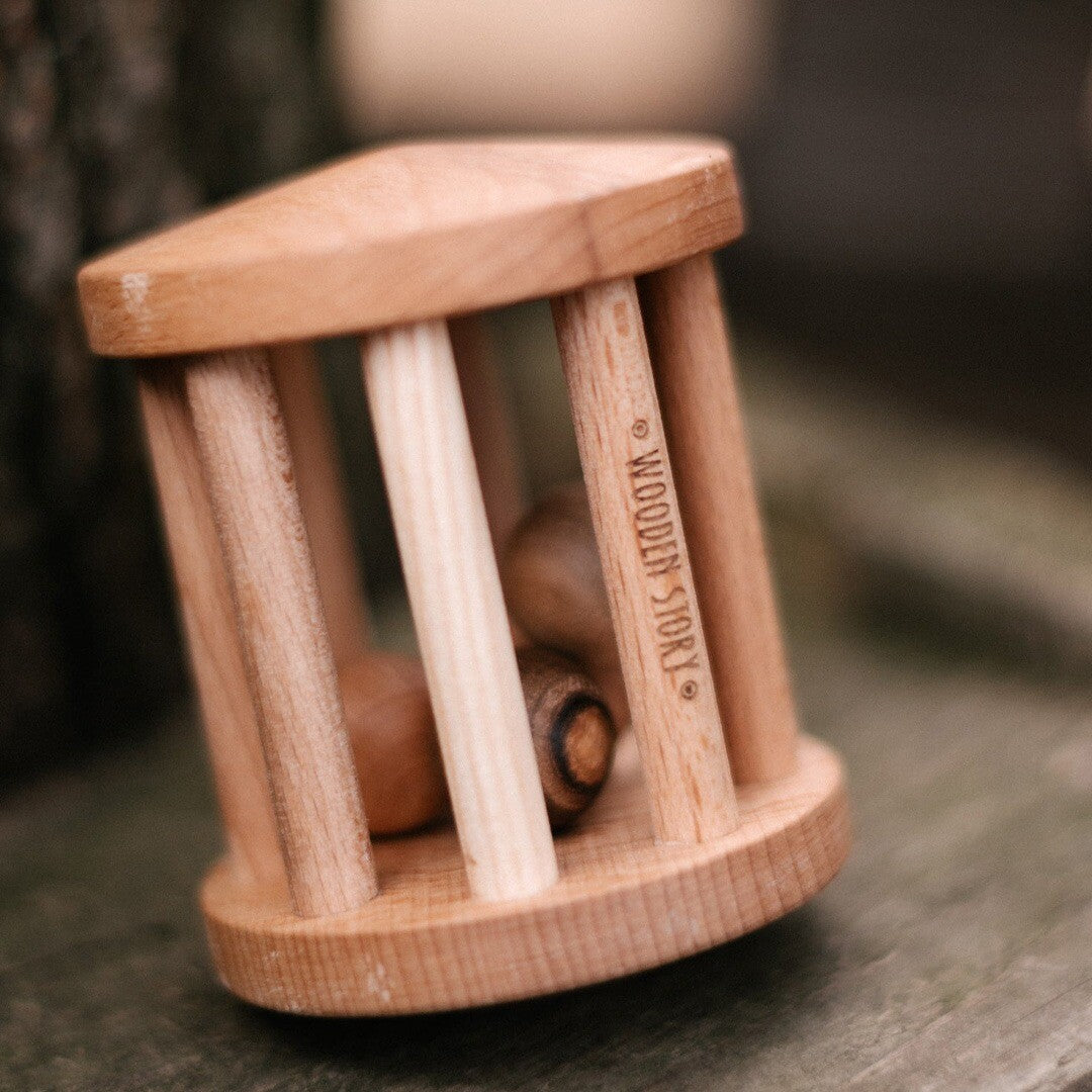 Close-up van de Wooden Story houten rammelaar met het merklogo gegraveerd op een van de spijlen.