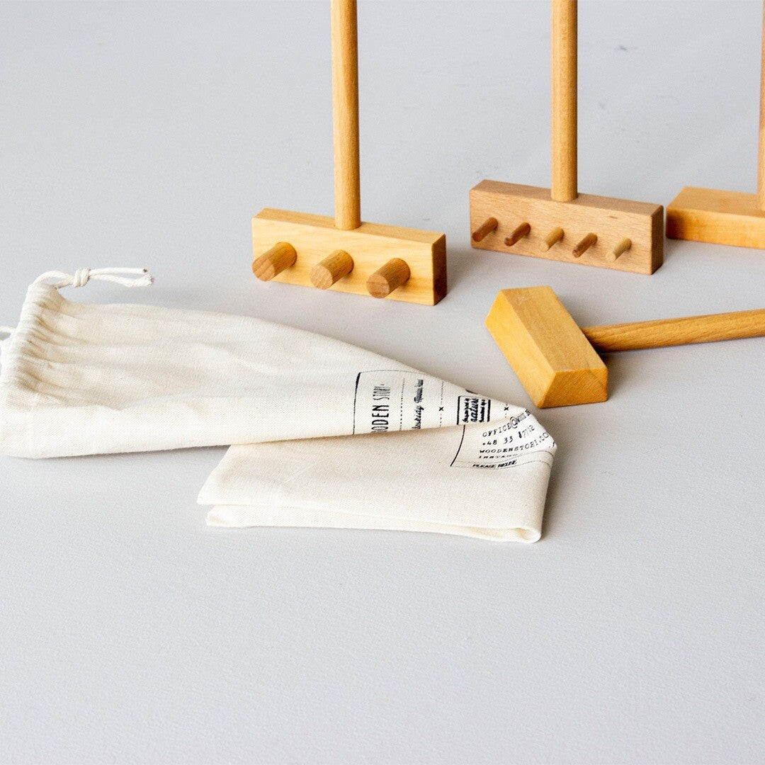 Drie Wooden Story houten speelbak accessoires en een witte stoffen zak op een grijze ondergrond.