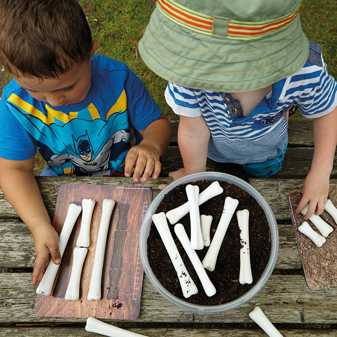 Twee kinderen spelen buiten met Yellow Door educatieve flashkaarten en witte dinosaurusbotten op een houten tafel.