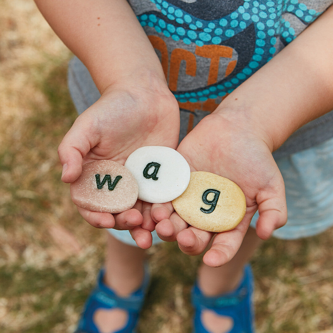 Kinderhanden houden drie Yellow Door alfabetstenen met de letters 'w', 'a' en 'g' vast.