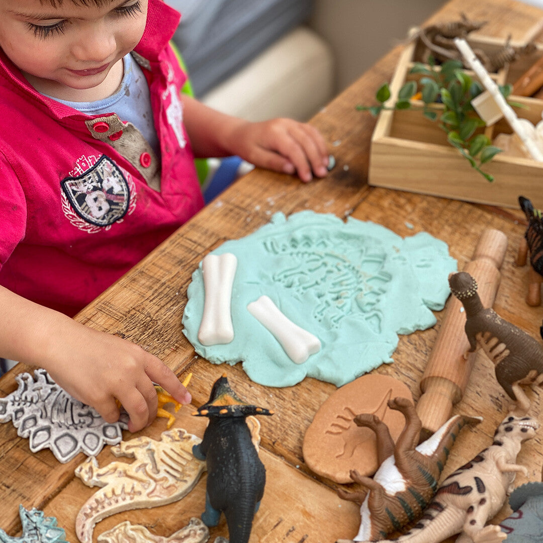 Een kind speelt met Yellow Door dinosaurusbotten op blauwe klei met een dinosaurusafdruk.