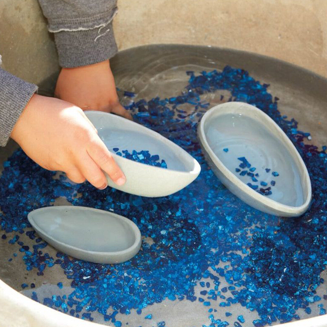 Kinderhanden spelen met yellow door gietkommen in een bak met water en blauwe glaskiezels.