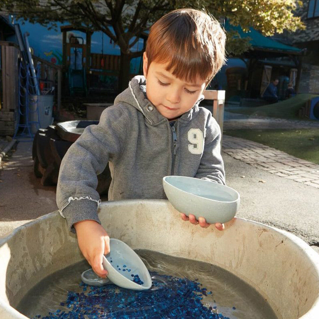Een jongen schept blauwe glaskiezels met een yellow door gietkom uit een waterbak.