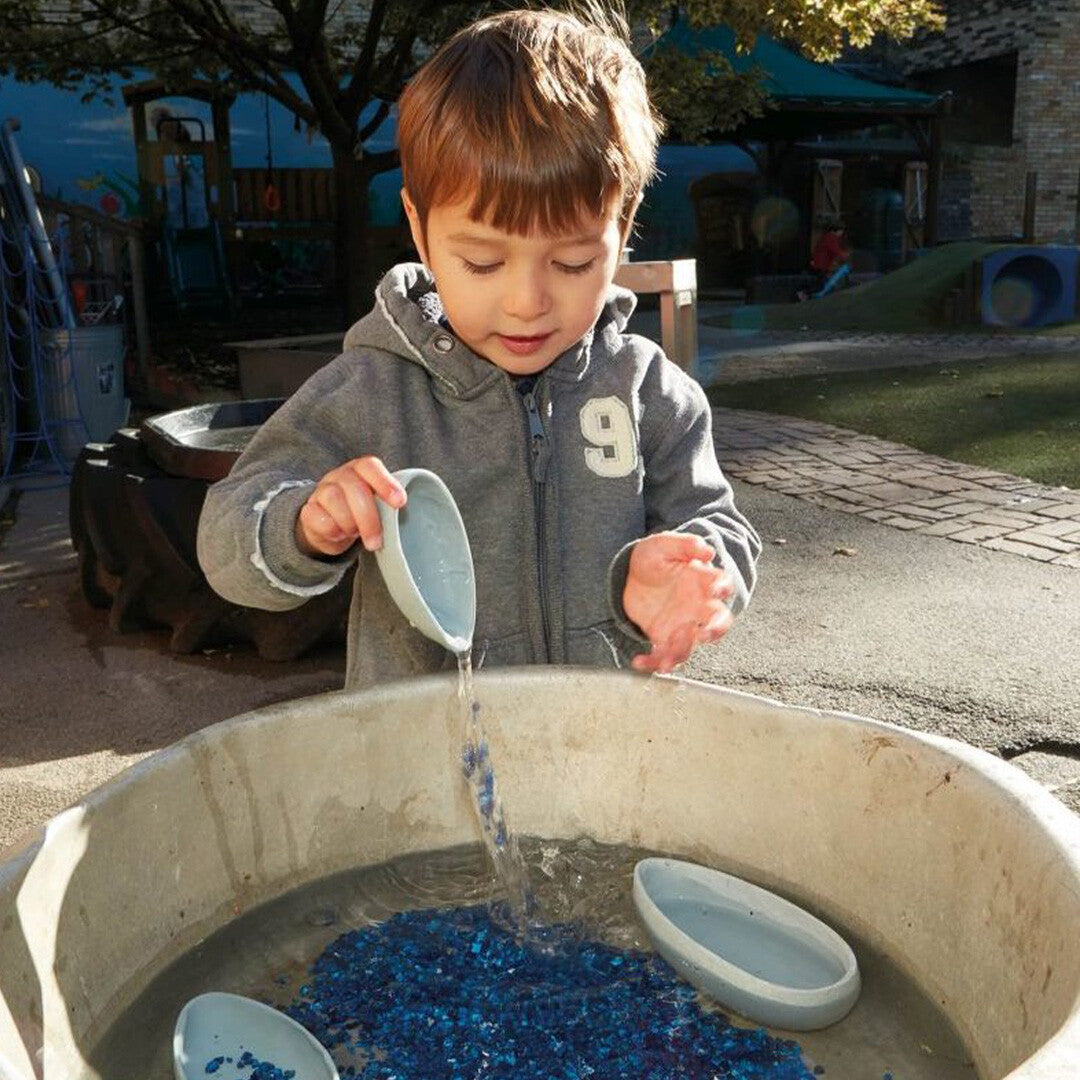 Een jongen giet water en blauwe glaskiezels uit een yellow door gietkom in een waterbak.