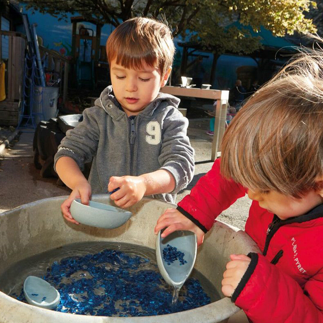 Twee jongens spelen samen met yellow door gietkommen in een waterbak met blauwe glaskiezels.