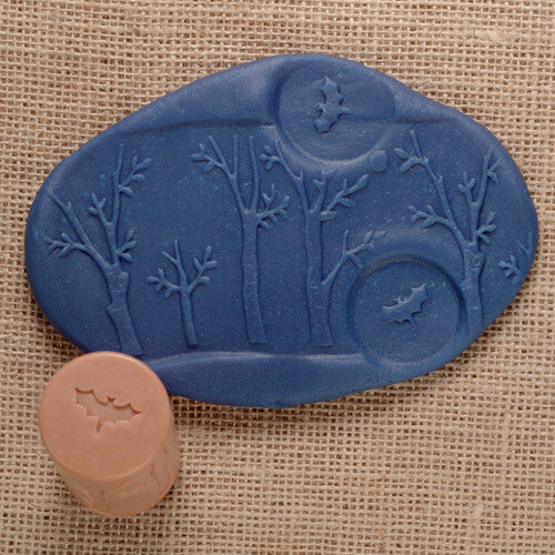 Een blauwe kleiafdruk van een boslandschap met bomen en vleermuizen, naast een beige Yellow Door kleistempel met een vleermuispatroon.