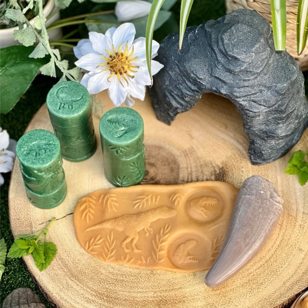Drie groene Yellow Door kleistempels, een kleiplaat met dinosaurusafdrukken en decoratieve elementen op een houten schijf.