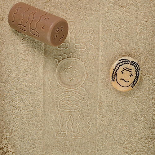 Een beige Yellow Door kleistempel heeft een afdruk van een verdrietige figuur achtergelaten in het zand.