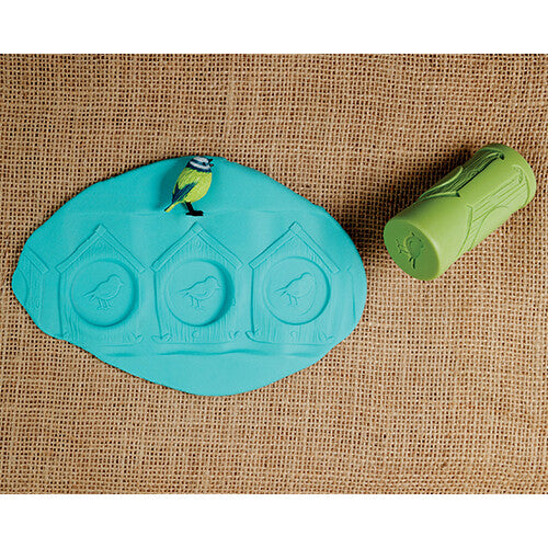 Een groene Yellow Door kleistempel naast een blauwe klei-afdruk van drie vogelhuisjes met een vogelfiguur erop.