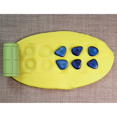 Een groene Yellow Door kleistempel naast een gele klei-afdruk van geometrische vormen en blauwe steentjes.