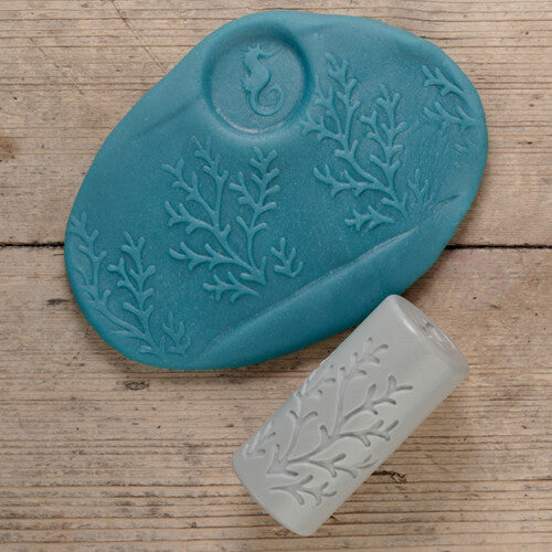 Een blauwe kleiafdruk met een zeepaardje en koraal, naast een grijze Yellow Door kleistempel met koraalpatroon.