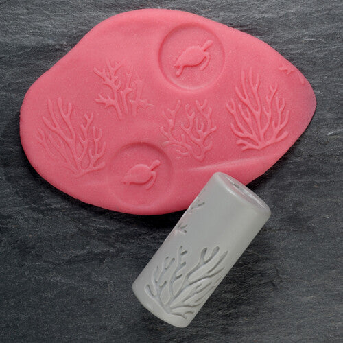 Een roze kleiafdruk met schildpadden en koraal, naast een grijze Yellow Door kleistempel met koraalpatroon.