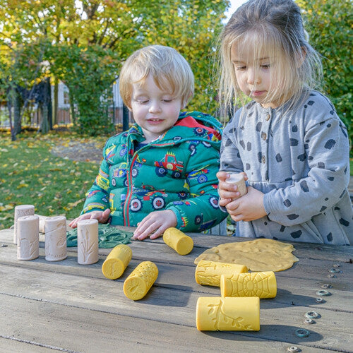 Twee jonge kinderen spelen buiten aan een houten tafel met de kleistempels en gele klei.