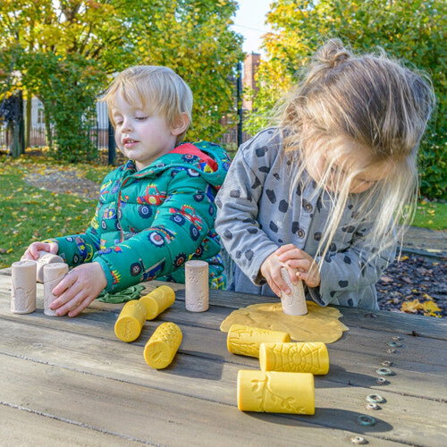 Twee jonge kinderen gebruiken de kleistempels om patronen te maken in gele klei op een houten tafel.